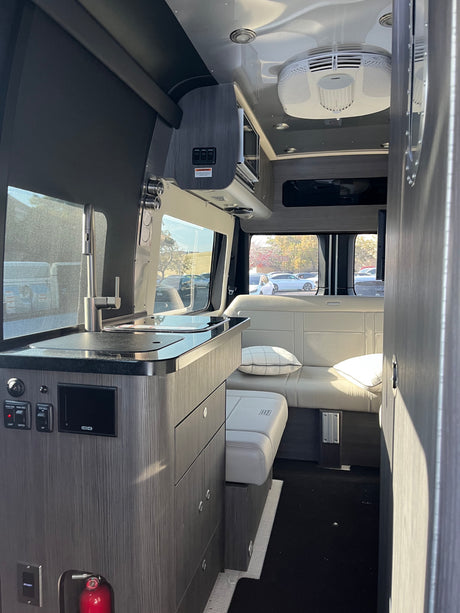 This RV rental showcases a bright, modern interior with a kitchen counter & sink on the left, and plush seating towards the rear.