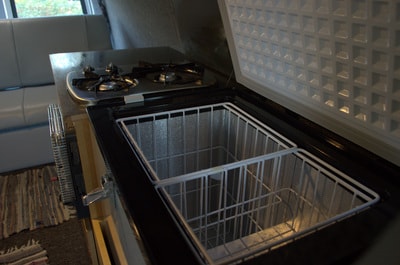 RV rental interior: compact kitchen with two-burner stove and open chest freezer showing storage baskets. — photo 9