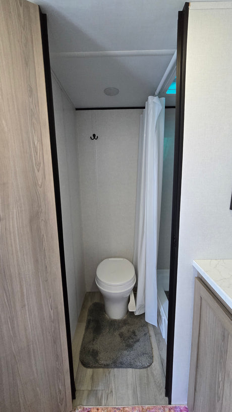 Compact RV rental bathroom with toilet, shower, vanity, and modern light wood-grain accents.