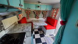 Vibrant vintage RV rental interior with teal cabinets, red dinette, marble-look table, and classic checkered floor.