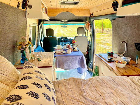 Cozy rv rental interior: dining table set, kitchen, bed, and view to vineyard. Perfect for travel adventures!