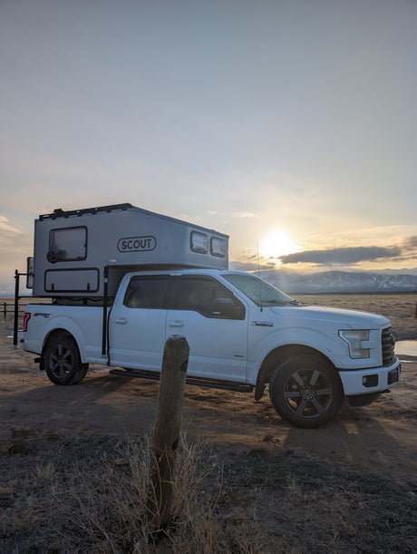 White Ford F-150 with Scout truck camper, ready for an RV rental adventure. Sunrise over mountains.