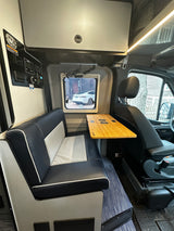 RV rental interior: Modern black and white seating, bamboo table with cup holders, and control panel. Window shows car.