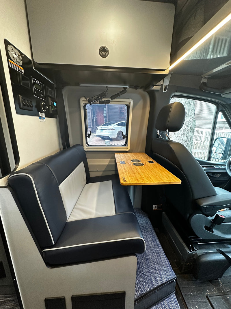RV rental interior: Modern black and white seating, bamboo table with cup holders, and control panel. Window shows car. — photo 10