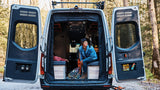 Experience van life with rv rental. Woman relaxing inside a converted camper van, surrounded by nature and climbing gear.