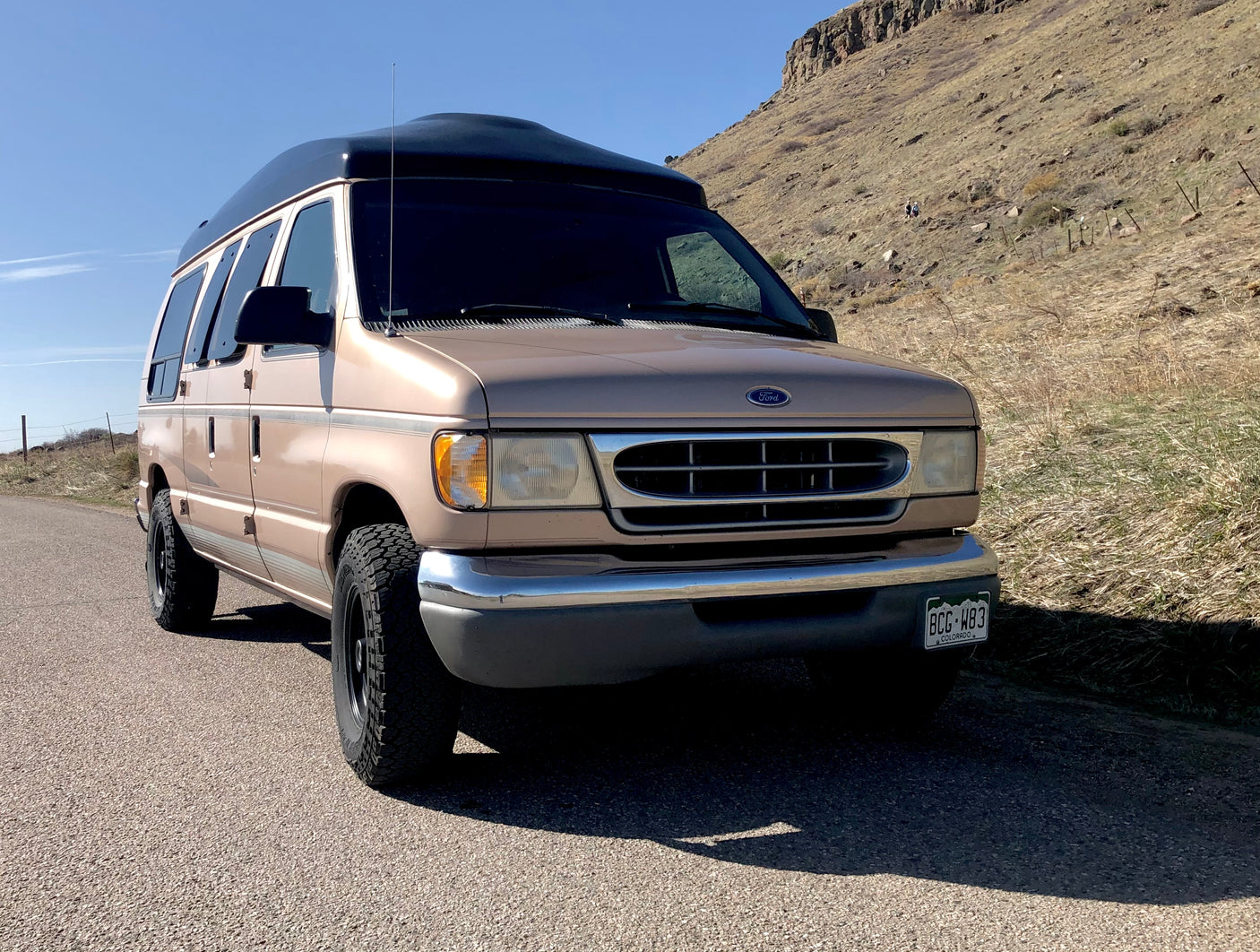Tan Ford high-top van, perfect for RV rental off-road adventures. Seen on a road near Colorado hills.