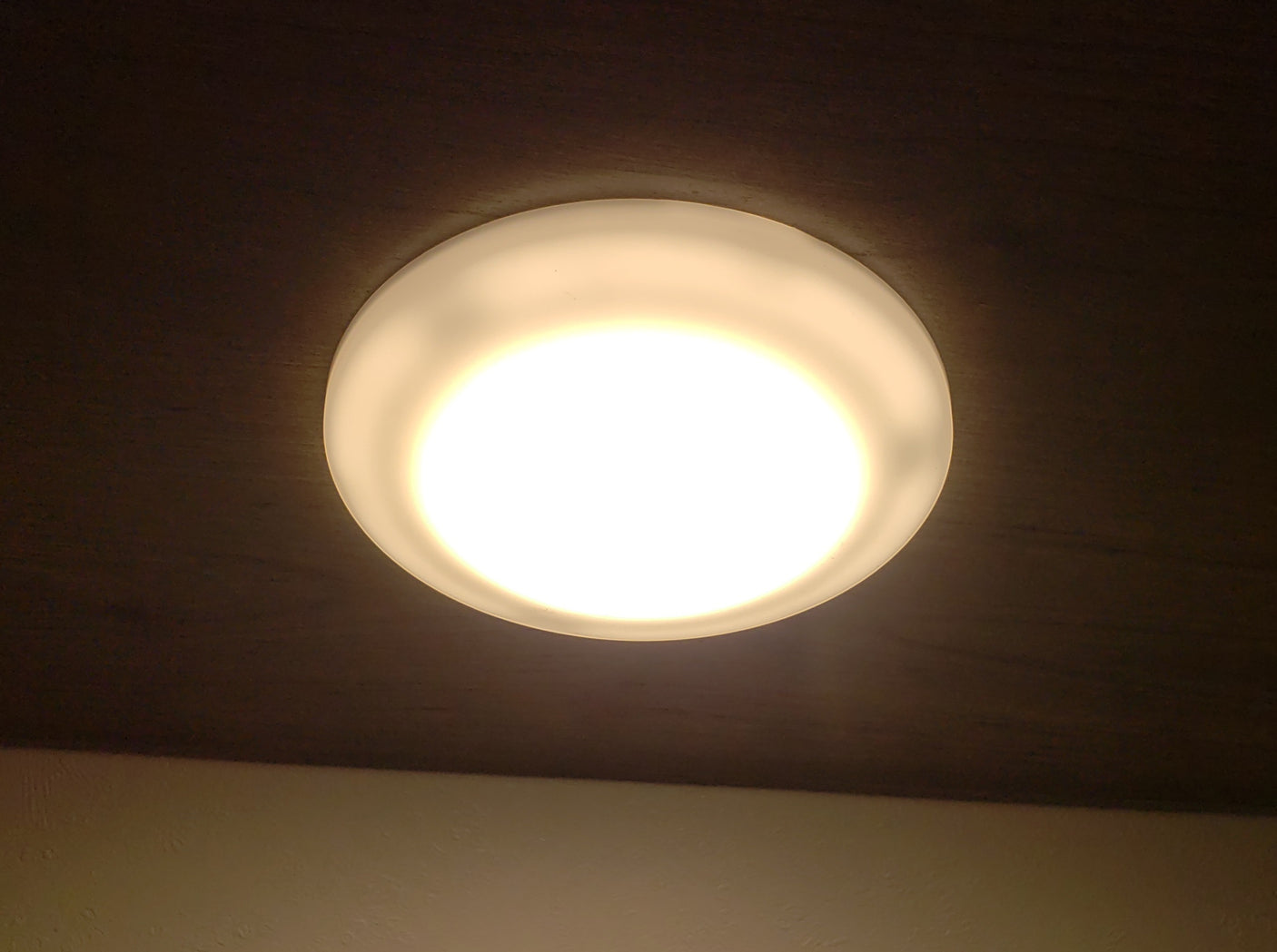 A warm, round ceiling light fixture brightens an RV rental space, mounted on a dark wooden ceiling.