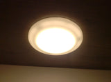 A warm, round ceiling light fixture brightens an RV rental space, mounted on a dark wooden ceiling.