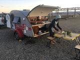 Person cooks at an outdoor kitchen setup of a gray teardrop RV rental, showcasing compact camping.
