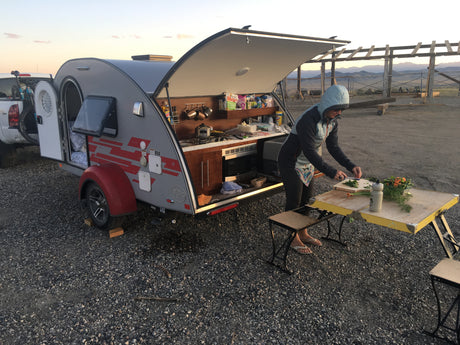 Person cooks at an outdoor kitchen setup of a gray teardrop RV rental, showcasing compact camping.