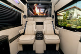 Luxury RV rental interior featuring cream quilted leather captain's chairs, center console, large screen with a digital fire, and window views.