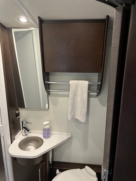 RV rental wet bath with corner sink, mirror, wall cabinet, towel bar, and toilet. Practical, compact design for travel.