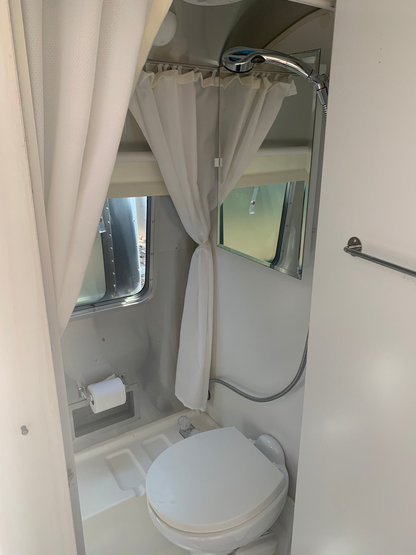 Bright RV rental Airstream bathroom: toilet, shower, curtains, mirror. A clean, compact space.
