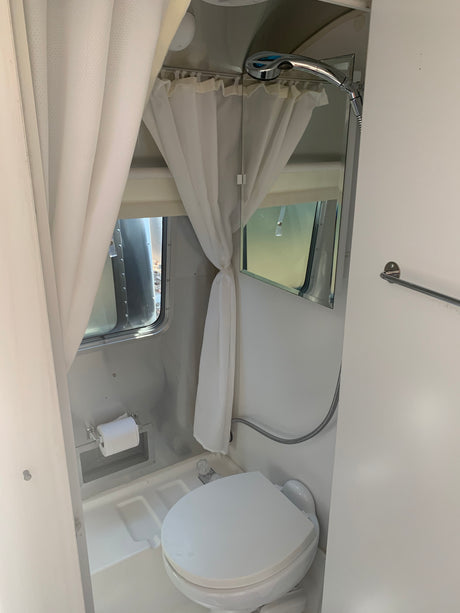 Bright RV rental Airstream bathroom: toilet, shower, curtains, mirror. A clean, compact space.