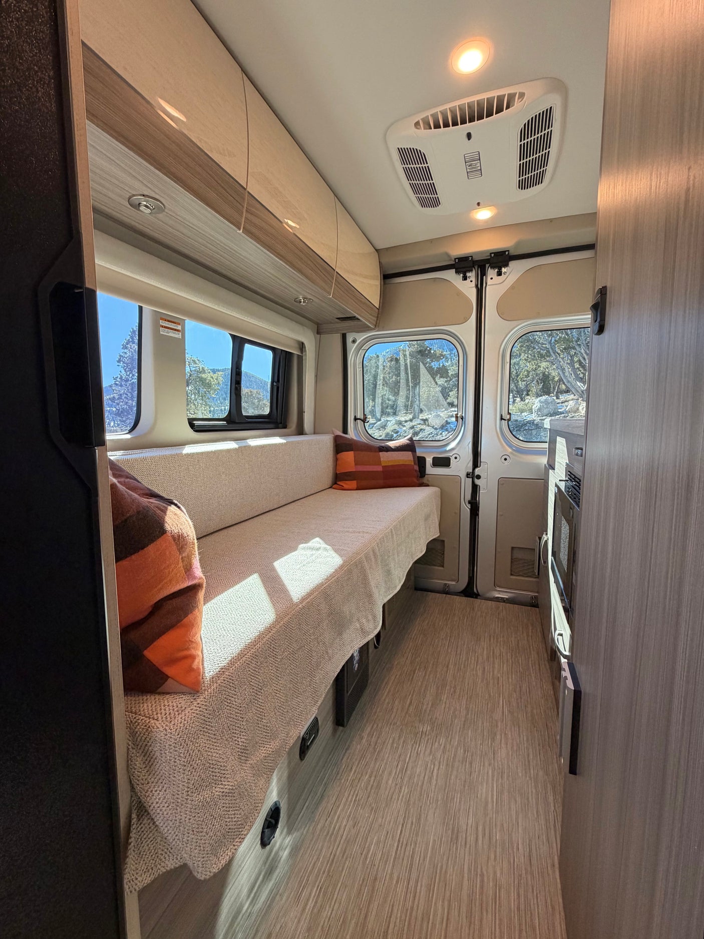Bright RV rental interior: comfy bench with cushions, scenic mountain views from windows, kitchenette, & overhead AC. Perfect for road trips.