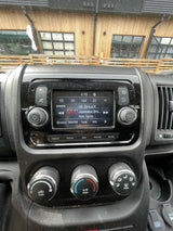 Inside an RV rental, showing the dashboard with an infotainment screen, climate controls, and a view of a modern building.