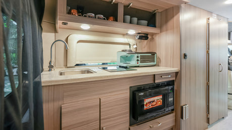 A bright, well-appointed RV rental kitchen features a sink, microwave, toaster oven, coffee maker, and ample storage.