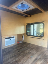Clean RV rental interior: wood walls, AC, ceiling fan, and window. Ready for your comfortable travels.