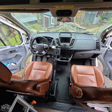 Inside a modern RV rental van: spacious front cabin with brown leather captain's chairs and a clean dashboard.