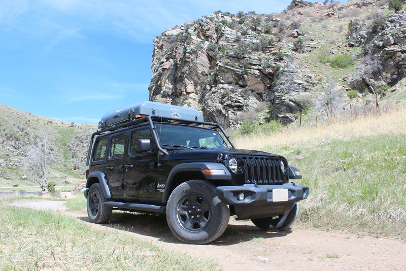 Black Jeep Wrangler with a rooftop tent on a dirt path, flanked by rocky mountains and dry grass. Ideal for an RV rental trip. — photo 12