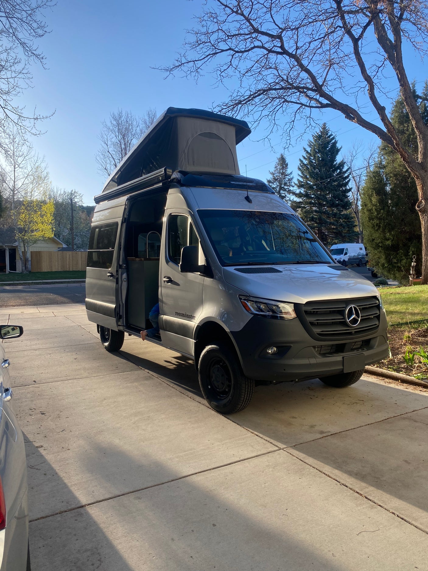 A grey Mercedes Sprinter camper van with a raised pop-top and open side door, perfect for an rv rental adventure.