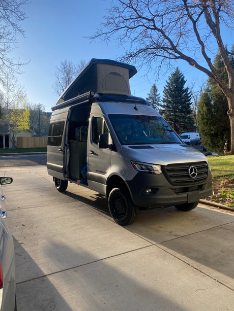 A grey Mercedes Sprinter camper van with a raised pop-top and open side door, perfect for an rv rental adventure.