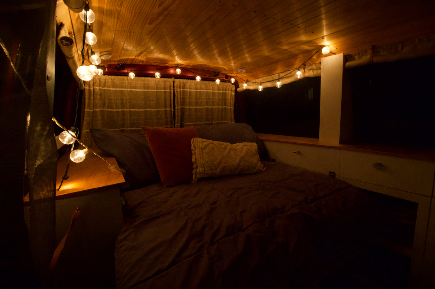 Cozy RV rental interior with a comfortable bed, warm string lights, and a charming wooden ceiling.