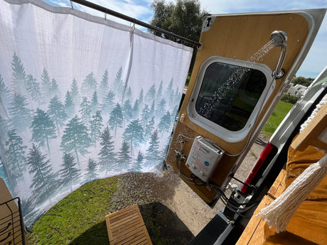 Experience an outdoor RV rental shower! This setup features a forest curtain, hot water heater, & spray from the van's rear.