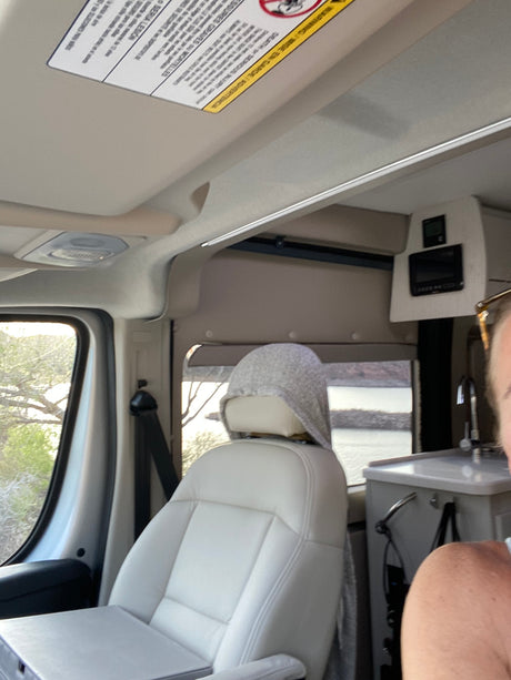 Cozy RV rental interior with a passenger seat, a glimpse of the mobile kitchen, and a beautiful lake view outside.