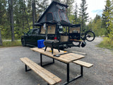 This custom truck **RV rental** features an overlanding tent, a full outdoor kitchen, and a bike mount at a campsite.