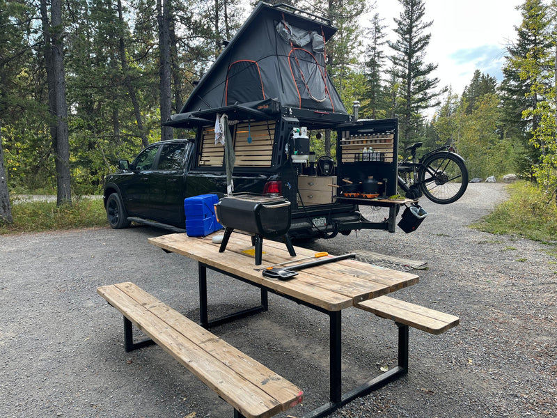 This custom truck **RV rental** features an overlanding tent, a full outdoor kitchen, and a bike mount at a campsite. — photo 12