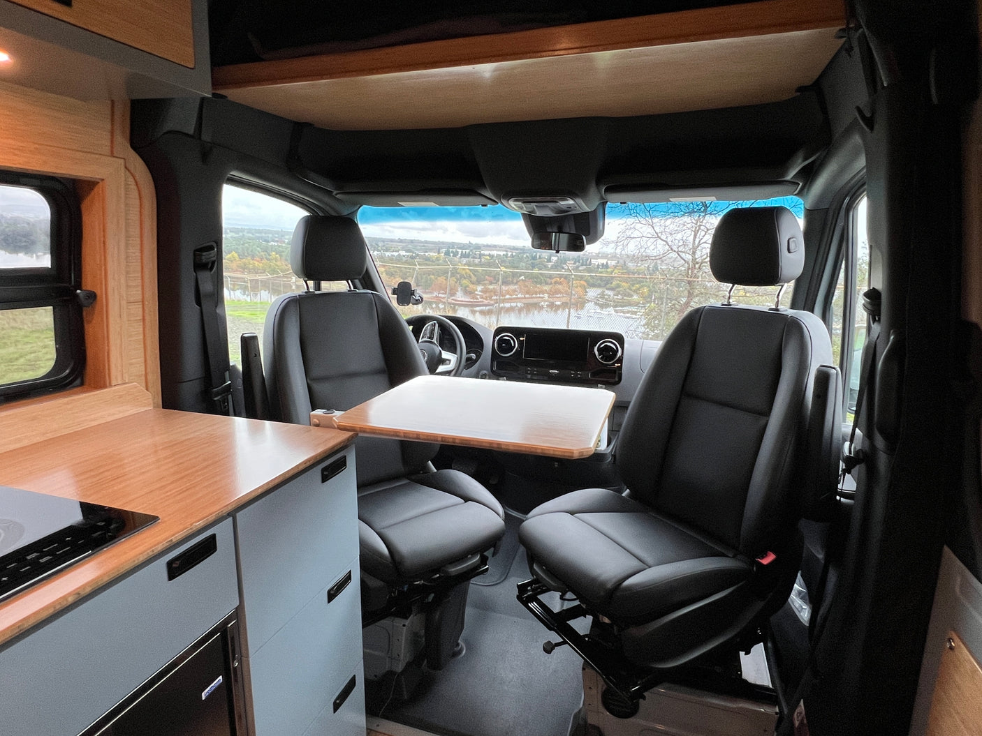 Inside this RV rental, front swivel seats face a portable table and kitchenette, offering scenic views for travelers.