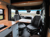 Inside this RV rental, front swivel seats face a portable table and kitchenette, offering scenic views for travelers.