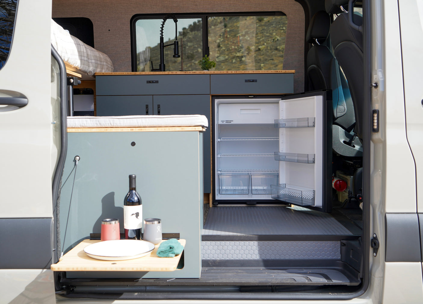 Inside an RV rental, showing a custom camper van interior with kitchenette, open fridge, and a prepared fold-out table.
