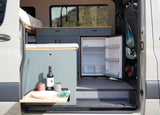 Inside an RV rental, showing a custom camper van interior with kitchenette, open fridge, and a prepared fold-out table.