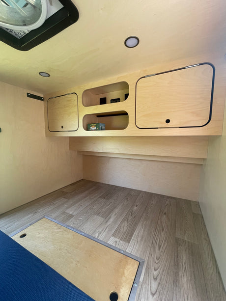 Clean and bright RV rental interior showcasing light wood paneling, built-in storage, and modern wood-look flooring.