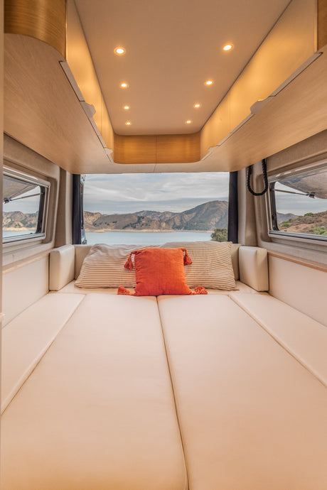 Cozy RV rental interior featuring a comfortable bed overlooking a panoramic lake and mountain view. Relaxing travel.