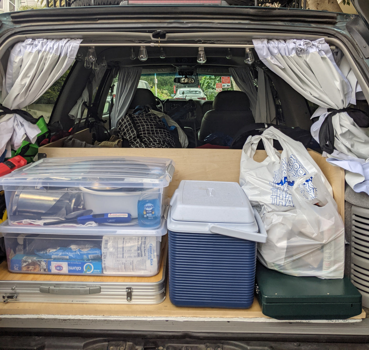 Organized **rv rental** trunk setup for car camping, with kitchen gear, food storage, cooler, stove, and privacy curtains.