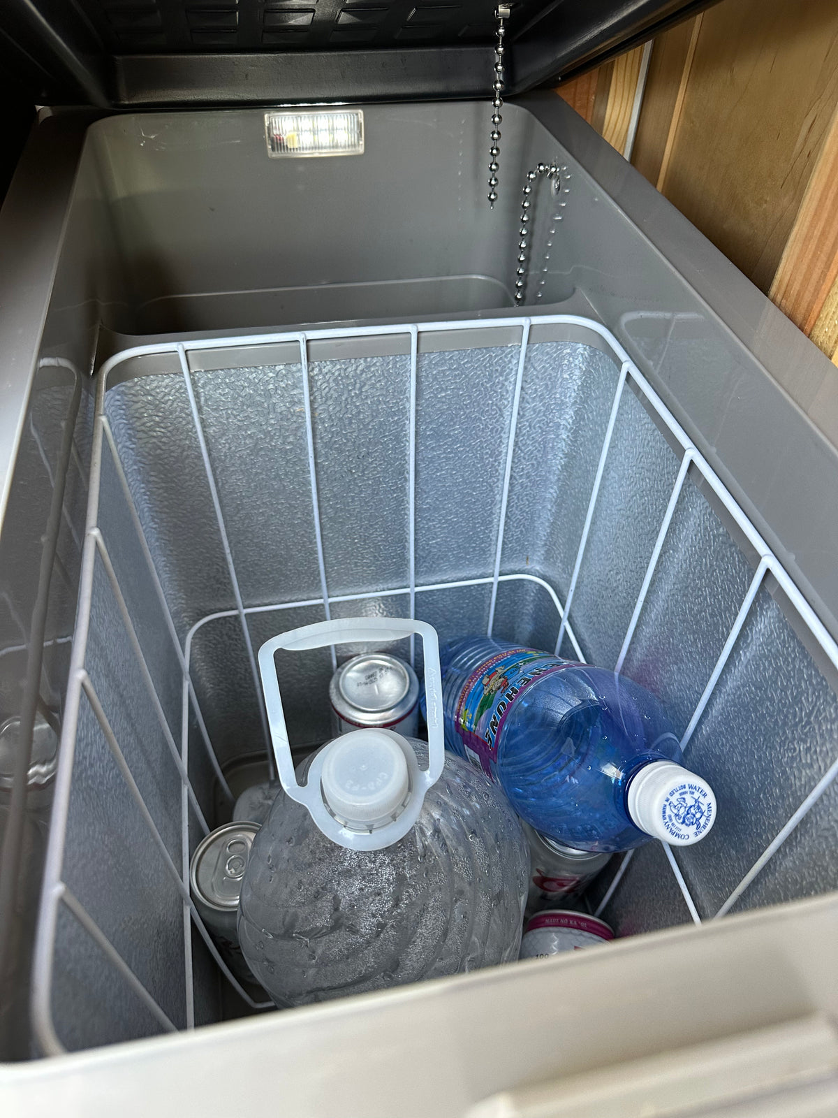 Cooler inside an RV rental, stocked with drinks: water jugs, Menehune water bottle, and cans. Essential for travel adventures. — photo 13