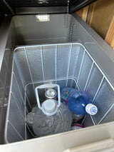 Cooler inside an RV rental, stocked with drinks: water jugs, Menehune water bottle, and cans. Essential for travel adventures.