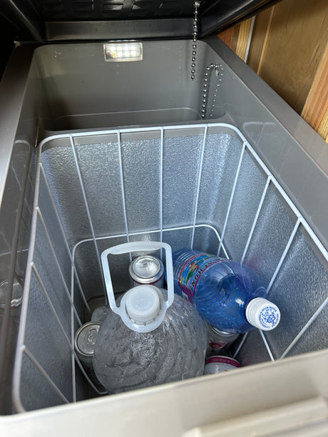 Cooler inside an RV rental, stocked with drinks: water jugs, Menehune water bottle, and cans. Essential for travel adventures.