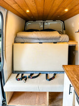 RV rental campervan interior: a cozy bed, convertible seating with seatbelts, and warm wood ceiling.