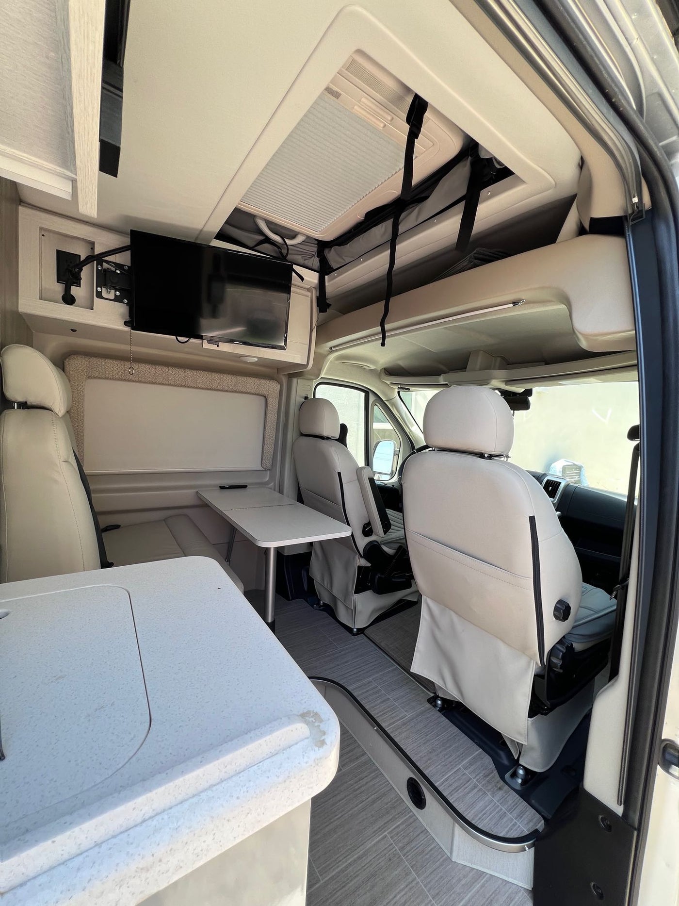  spacious camper van cockpit with driver/passenger seats & dashboard visible.|Inside a modern **rv rental**: light gray interior with kitchen — photo 4