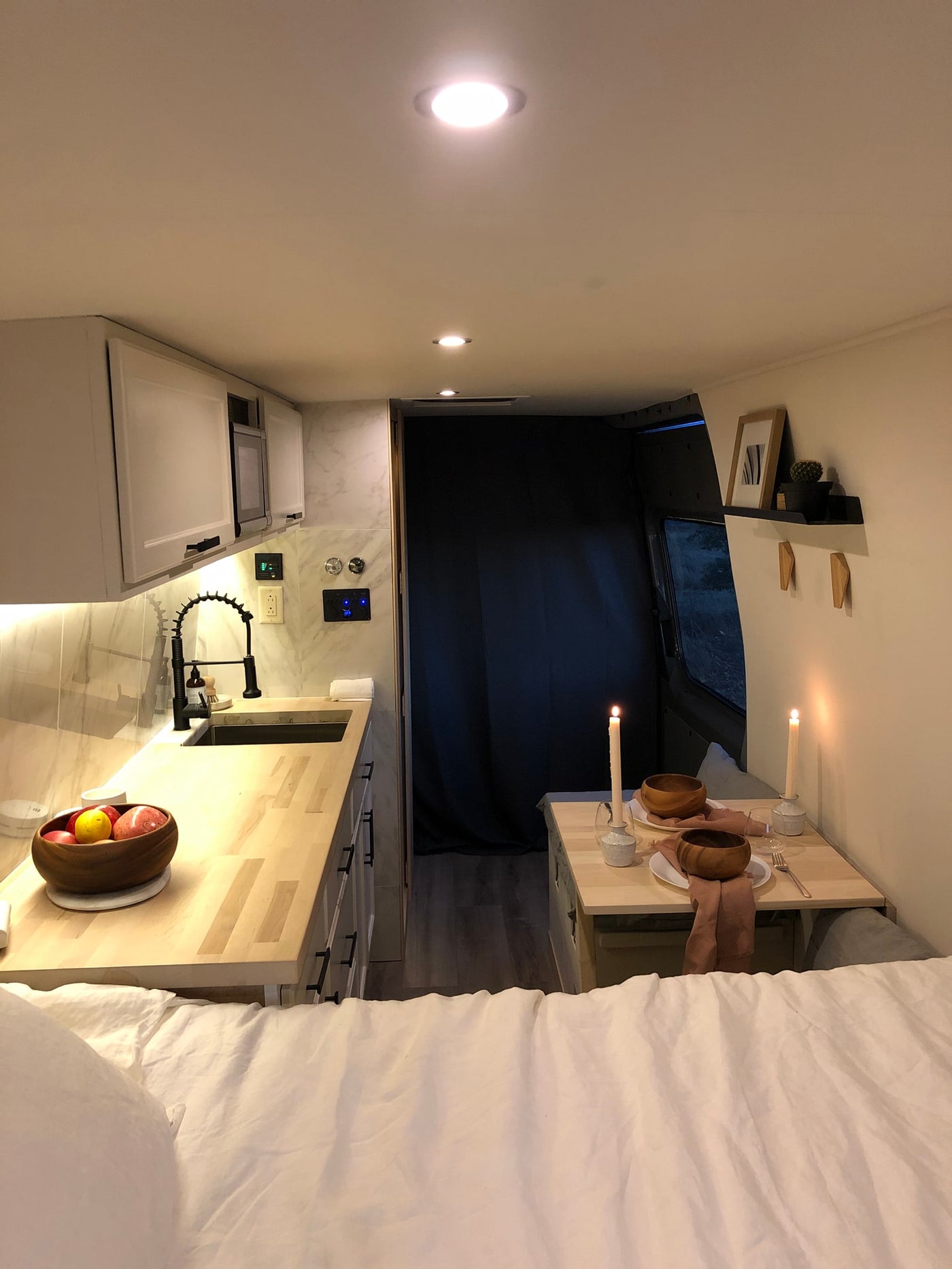 Experience comfort in this rv rental. Bright kitchen, cozy dining area with candles, and a large bed in foreground. — photo 6