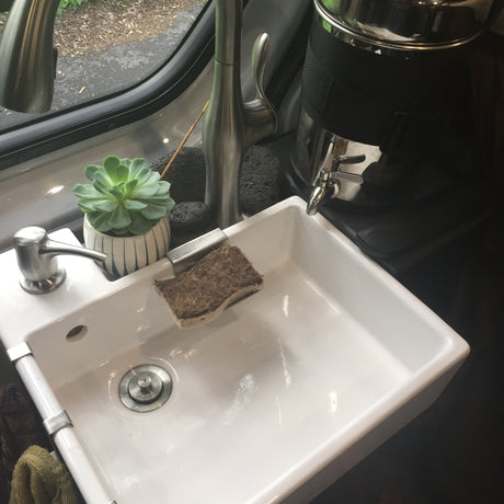 Bright sink with soap, sponge, and plant in an RV rental. Modern faucet and compact design for on-the-go living.