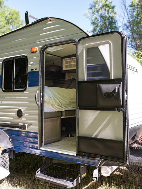 Open door of a compact rv rental camper with an interior bed and A/C unit, ready for your camping adventure.