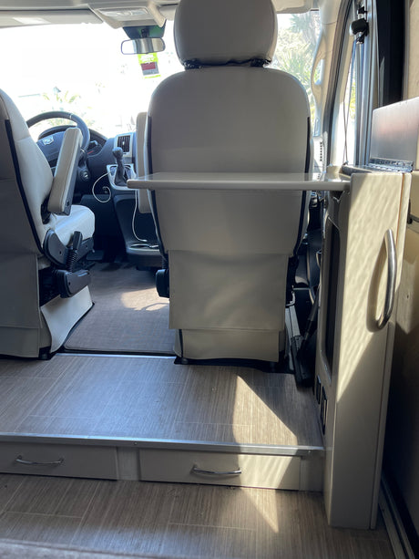 Inside an RV rental: swivel front seats with a mounted table, light flooring, and convenient storage drawers.