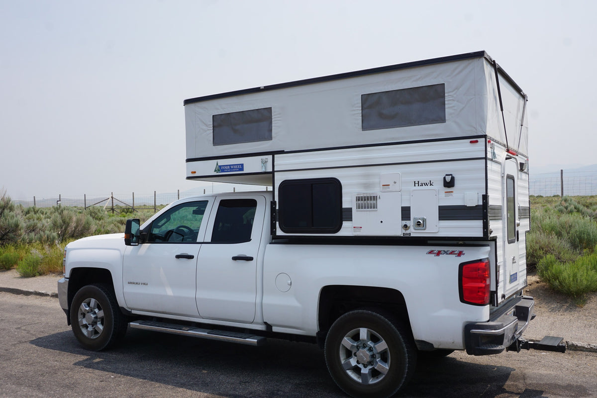 This white pickup truck with a raised Four Wheel Pop-Up Hawk truck camper is ready for an RV rental journey.