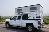 This white pickup truck with a raised Four Wheel Pop-Up Hawk truck camper is ready for an RV rental journey.