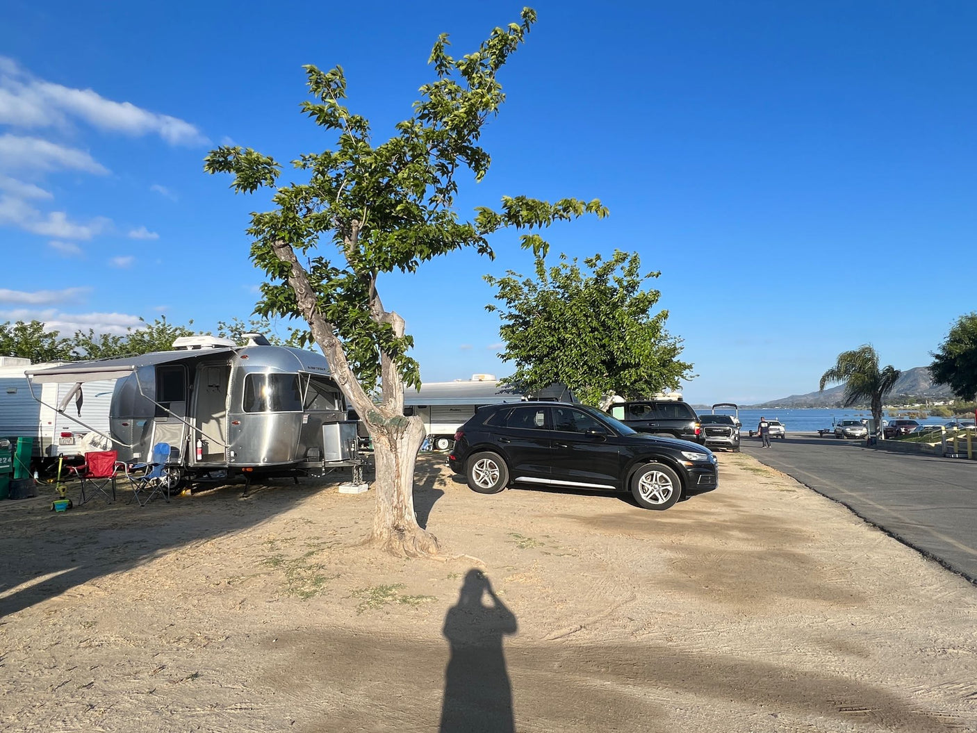 An Airstream rv rental and SUV parked at a lakeside campsite with clear blue skies and mountains, perfect for a relaxing trip.